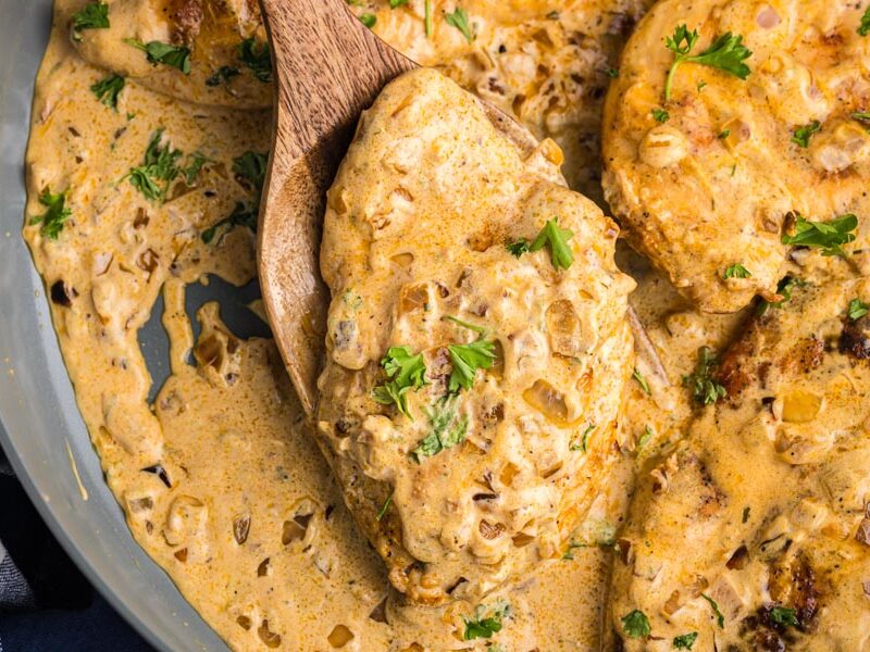 A wooden spoon holding a slice of creamy boursin chicken topped with parsley.