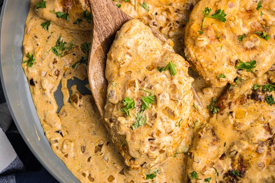 A wooden spoon holding a slice of creamy boursin chicken topped with parsley.