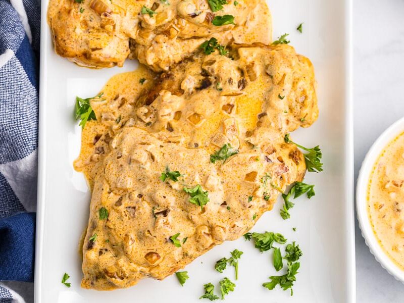 A serving platter with cooked, creamy chicken topped with a boursin cheese sauce and chopped parsley.