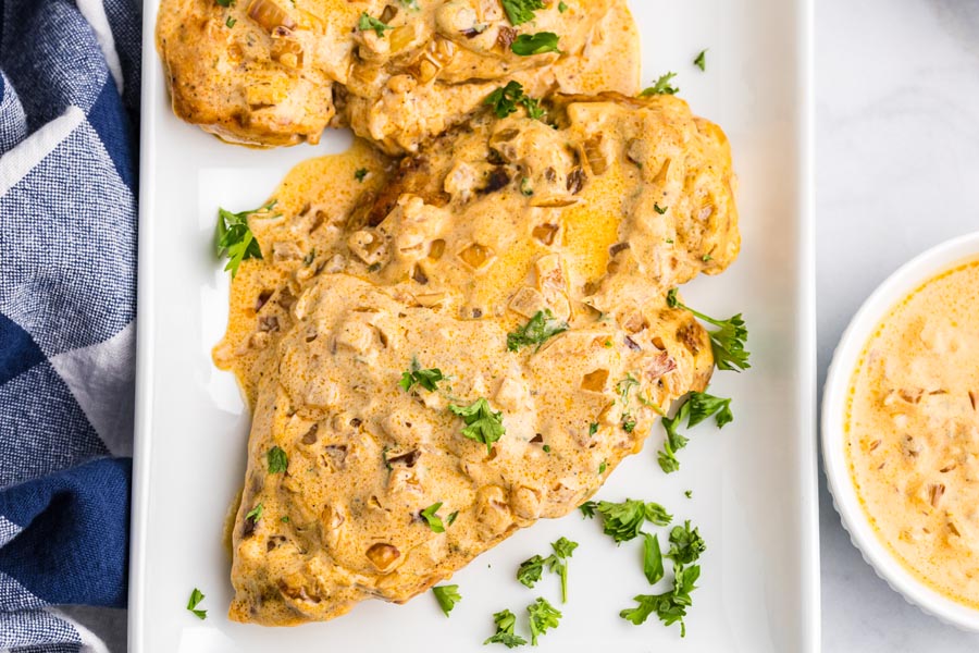 A serving platter with cooked, creamy chicken topped with a boursin cheese sauce and chopped parsley.