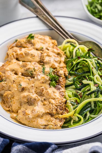 Sliced boursin chicken on a dinner plate next to a bed of cooked zucchini noodles.