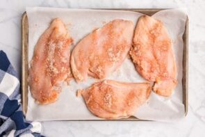 Four chicken cutlets sitting in a tray covered with seasoning.