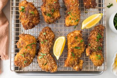 Crispy chicken cutlets on a wire rack topped with chopped parsley and lemon wedges near by.