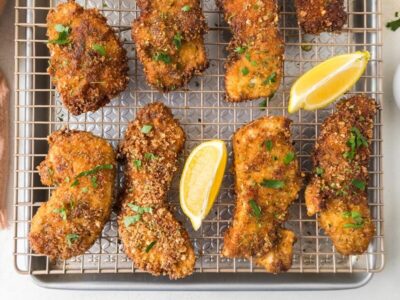 Crispy chicken cutlets on a wire rack topped with chopped parsley and lemon wedges near by.