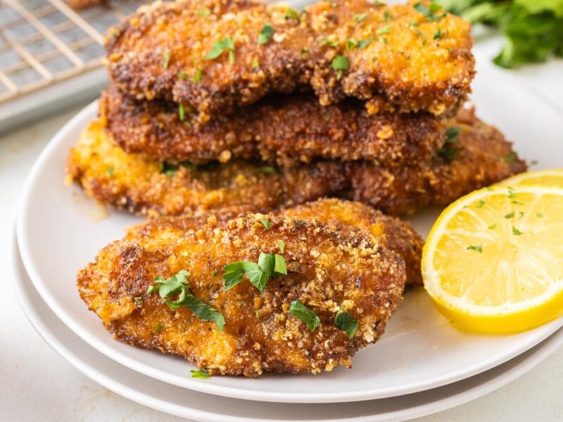 Breaded chicken cutlets on a plate with lemon slices.