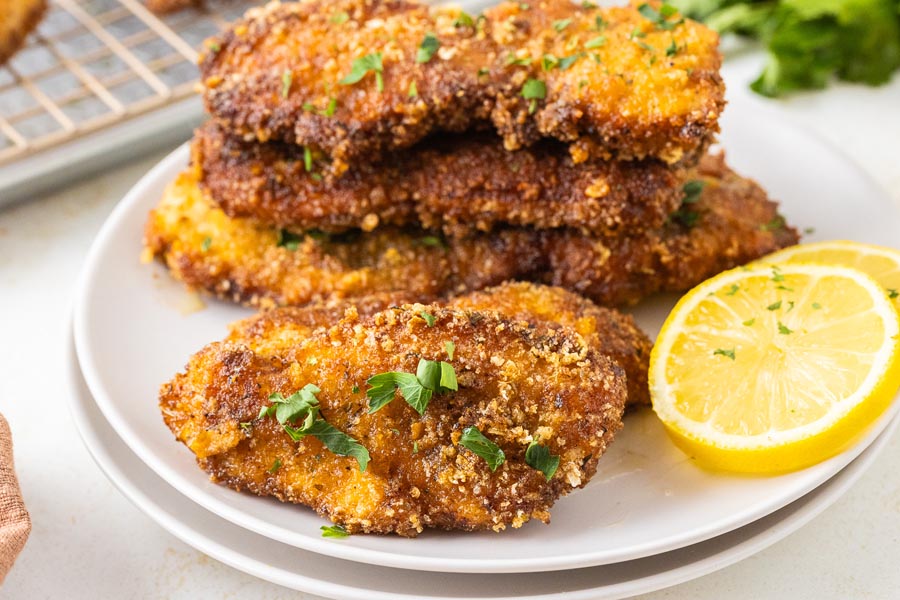 Breaded chicken cutlets on a plate with lemon slices.