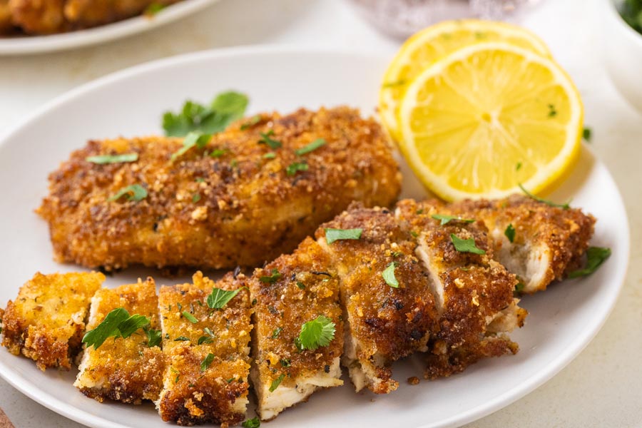 Sliced up keto chicken cutlets on a plate with lemon.