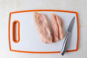 A few slices of chicken breast cut along the grain on a cutting board.