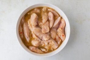 Chicken cutlets marinating in Italian dressing in a bowl.