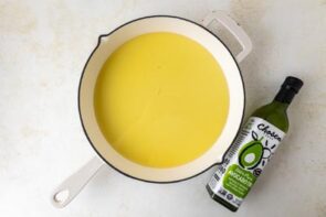 Avocado oil in a white skillet next to a bottle of avocado oil.