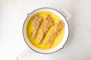 Frying three chicken cutlets in a skillet with avocado oil.