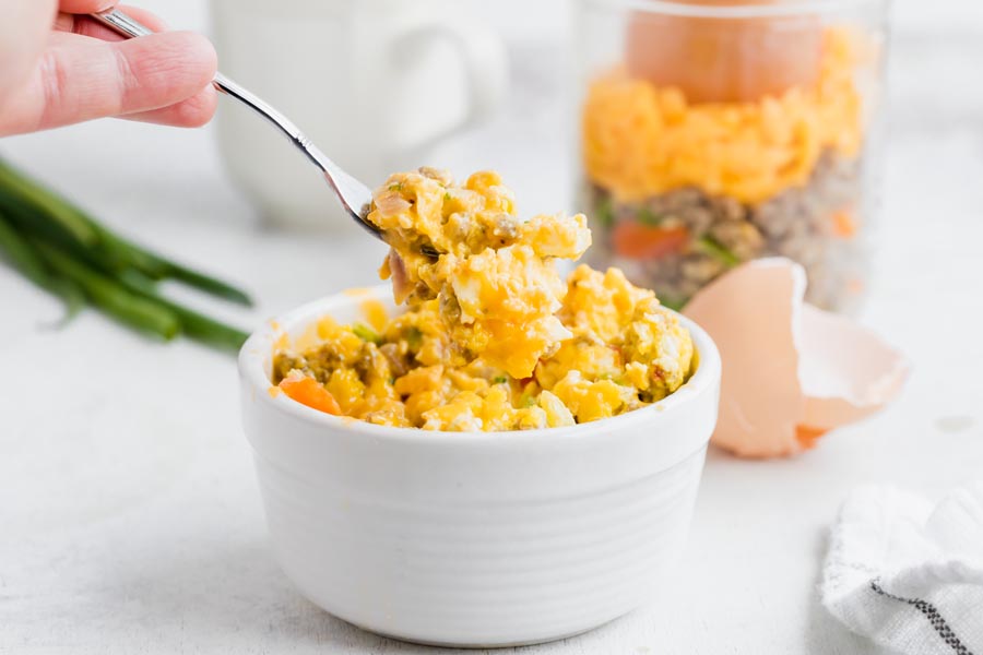 A hand taking out a forkful of scrambled eggs from a white bowl.