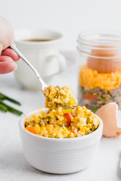 A forkful of sausage and egg scrambled over a bowl with more scrambled eggs.