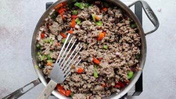 A mixture of ground sausage and pepper and onions with a spatula in the skillet.