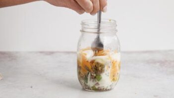 A fork stirring a scrambled egg inside a jar.