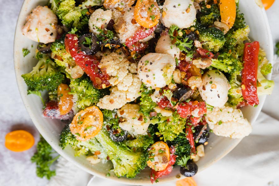 A colorful broccoli salad with cauliflower, cheese, tomatoes and roasted peppers.