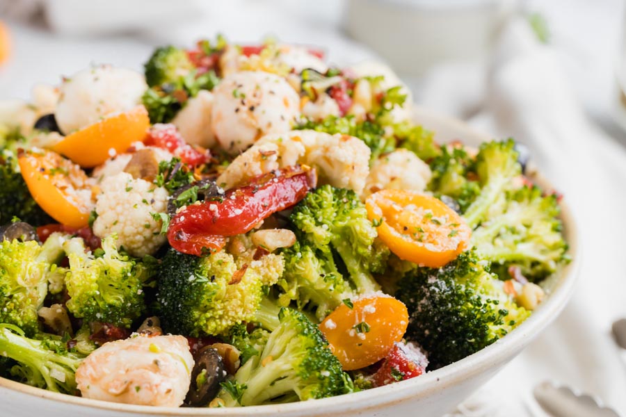 Broccoli salad in a bowl with slice tomato, red pepper slices, cauliflower topped with a zesty dressing and walnuts.
