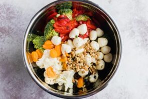 Looking down into a bowl with tomatoes, roasted red bell pepper, broccoli, cheese balls, cauliflower and chopped walnuts inside.