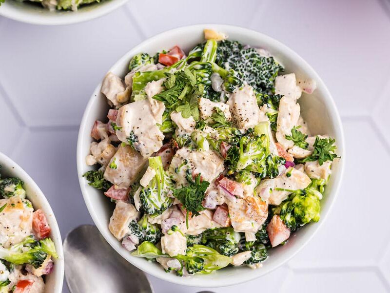 A bowl of creamy coated broccoli and chicken salad with bell pepper and onion.