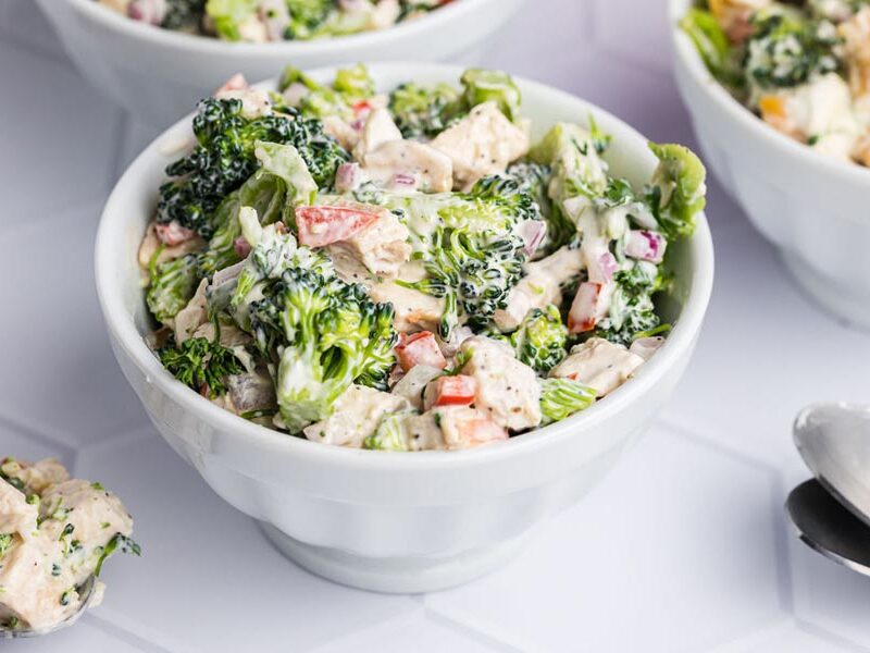 A small bowl of broccoli salad coated in a creamy dressing with chunks of chicken and red pepper.
