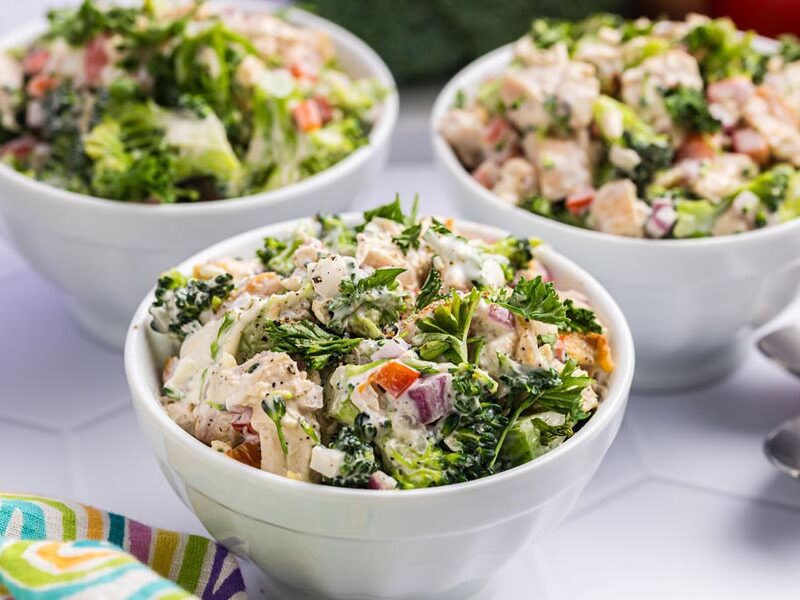 Three bowls of broccoli chicken salad topped with fresh parsley.