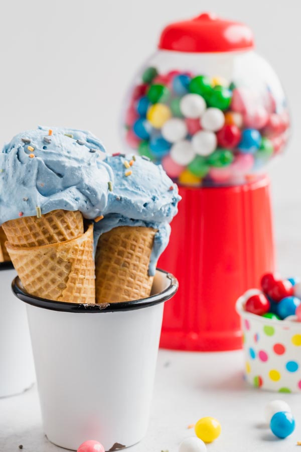 two blue ice cream cones in a white cup with a bubble gum machine in the background