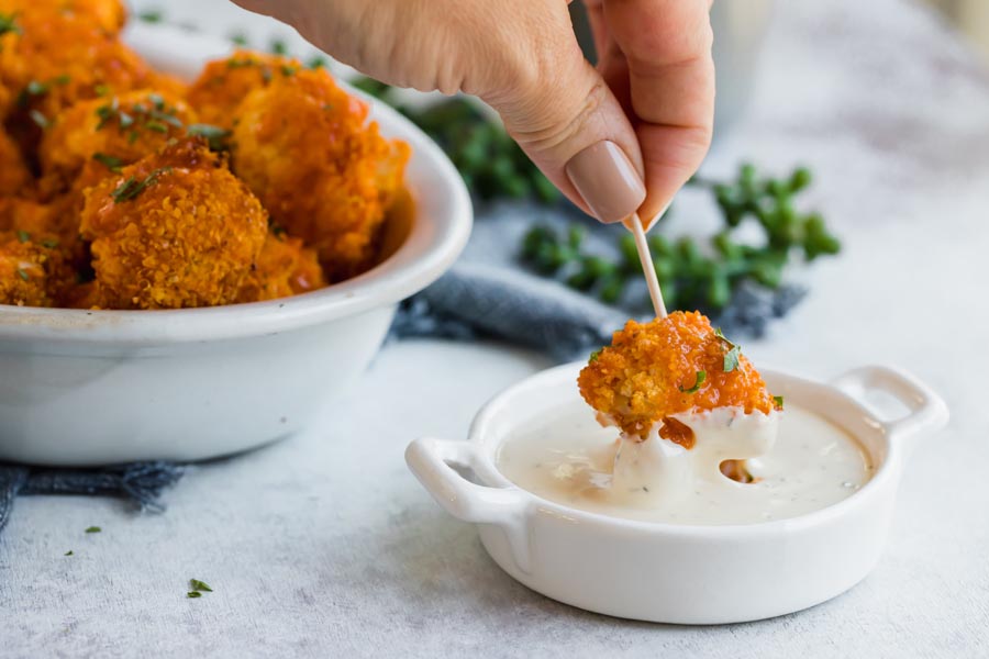 dipping cauliflower bite into ranch dressing with a toothpick