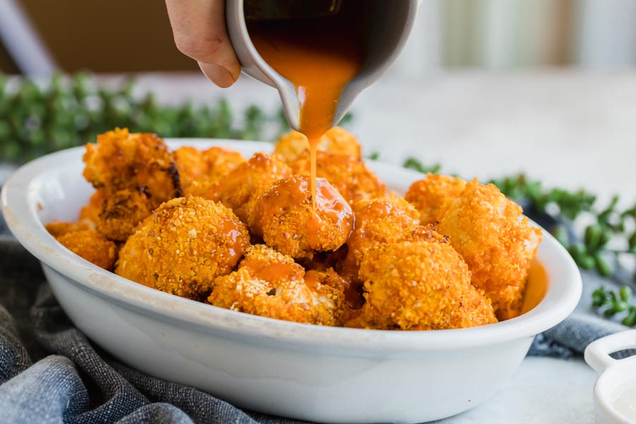 pouring spicy buffalo sauce from a boat onto crunchy roasted cauliflower