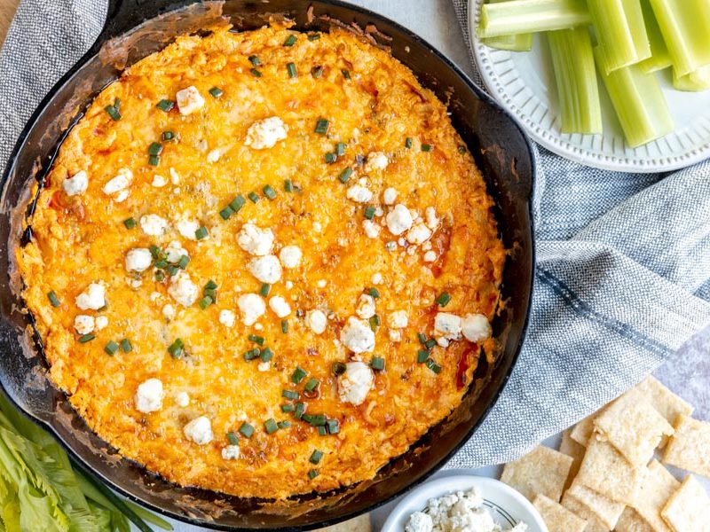 looking down onto a skillet with cheesy buffalo dip inside and celery sticks near by