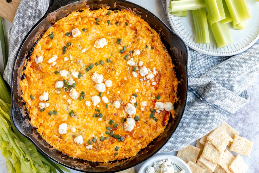 looking down onto a skillet with cheesy buffalo dip inside and celery sticks near by
