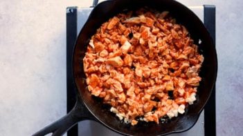 shredded chicken mixed with buffalo wing sauce in a cast iron skillet on a single burner