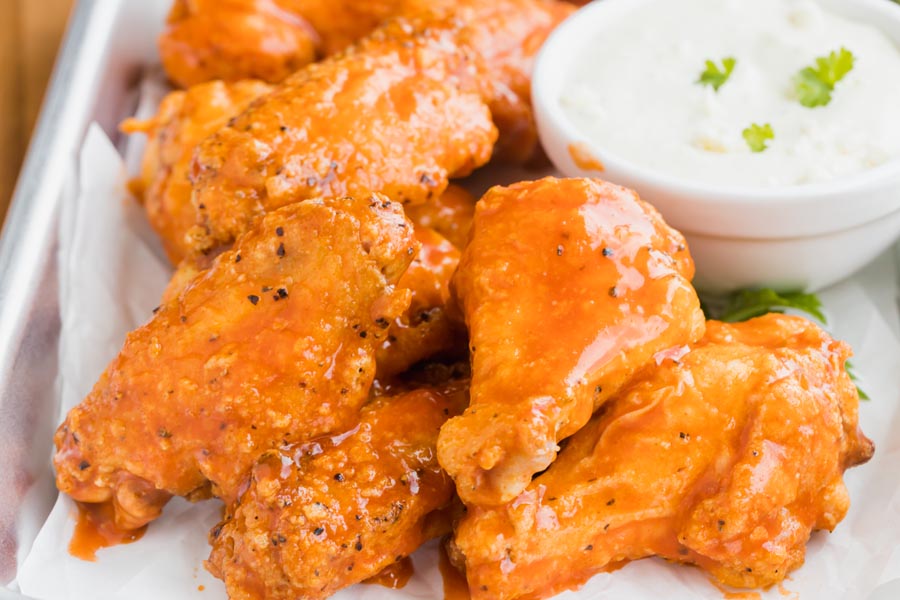 A pile of wings sauced with buffalo sauce next to a bowl a ranch dressing.