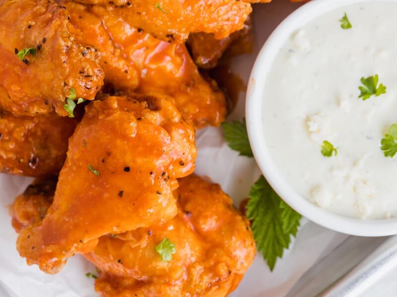 Small buffalo wings on a tray topped with parsley and next to a small bowl of blue cheese dressing.