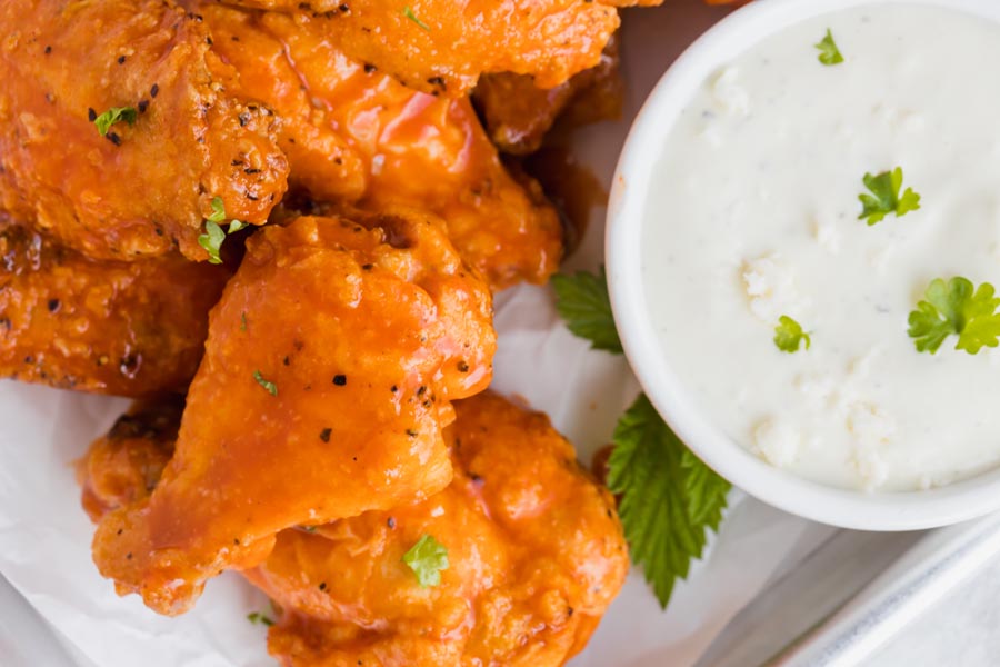 Small buffalo wings on a tray topped with parsley and next to a small bowl of blue cheese dressing.