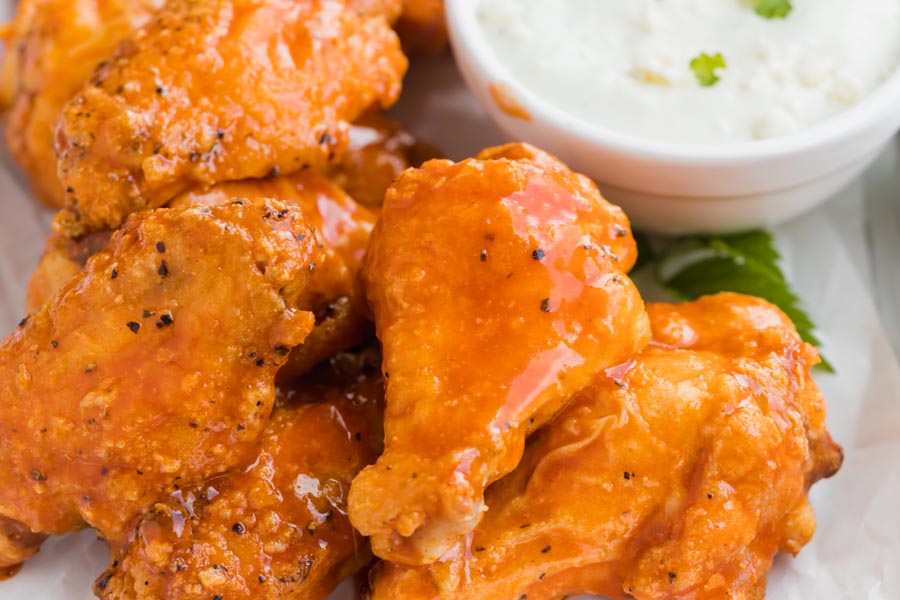 Close up of buffalo wings covered in hot sauce next to a small white bowl of blue cheese dressing.