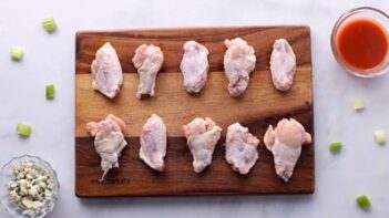 A cutting board with party wings lined up on it.