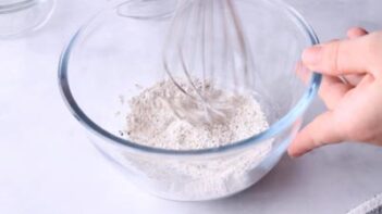 Whisking a mixture of baking powder and seasoning in a glass bowl.