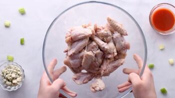 Two hands holding a bowl with baking powder coated wings.