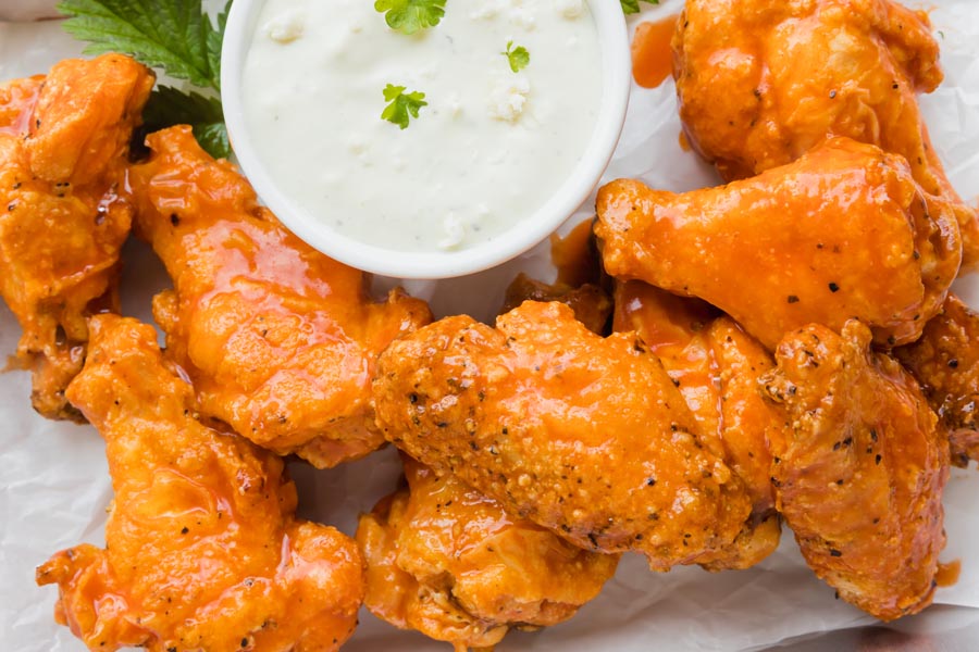 Juicy buffalo wings on parchment paper next to a small bowl of blue cheese dressing topped with parsley.