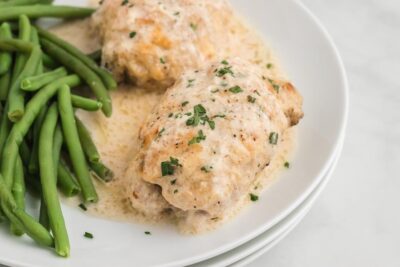 Juicy caesar dressing topped chicken thighs on a plate with steamed green beans.