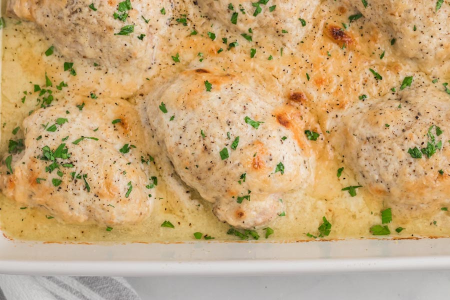 Chicken caesar casserole in a white casserole dish topped with chopped parsley.