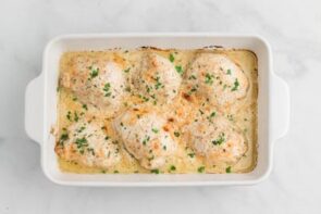 Baked chicken casserole in a baking dish with white sauce and topped with parsley.