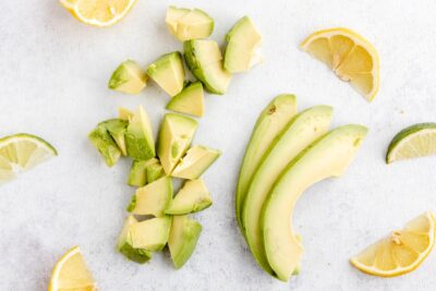slices and chunks of avocado surrounded by slices of lemon and lime
