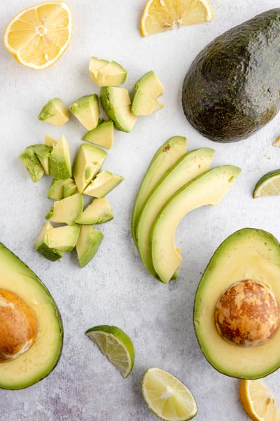 two avocado halves next to diced avocado and a few slices on a board