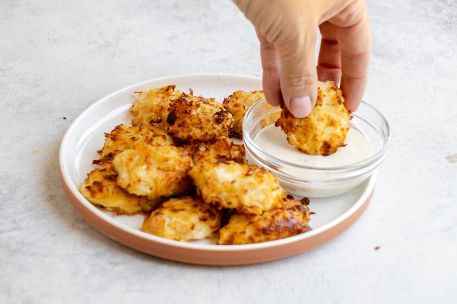 A hand dipping a crispy canned chicken nugget into a bowl of creamy ranch dressing.