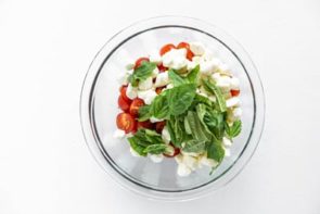 a clear bowl with fresh basil leaves over mozzarella cheese balls