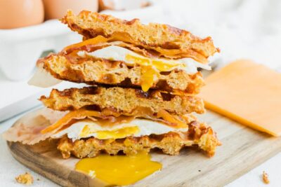 A waffle sandwich cut in half with yolk dripping out of the fried egg in the sandwich.