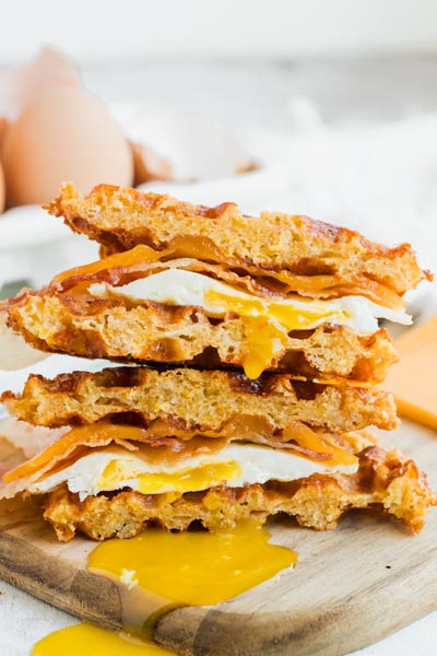 A sandwich cut in half, stack on itself with egg yolk dripping out and down onto a cutting board.