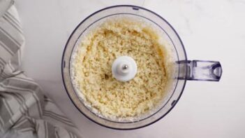 A food processor bowl with riced cauliflower inside.