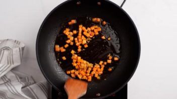 A skillet with diced carrots cooking in oil.